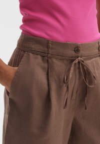 Pantalon en lin marron à coupe décontractée, avec poches latérales, taille à cordon de serrage et fermeture par bouton. Tissu texturé avec une finition douce.