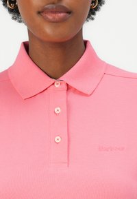 Roze polo shirt van gestructureerde stof, met een kraag, een placket met drie knopen en een reliëf "Barbour" logo op de borst.