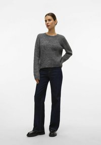 Pull en tricot gris à encolure ronde et manches longues, associé à un jean droit bleu marine et des chaussures noires. Design simple et texturé.