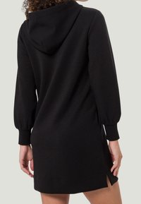 Robe à capuche noire avec manches longues bouffantes, poche kangourou, fentes sur les côtés et réalisée en un mélange de coton doux.