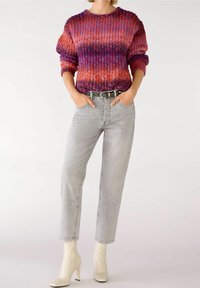 Stickad tröja med en gradient av röd, lila och orange nyanser, tillsammans med ljusgrå raka jeans och vita anklarstövlar.