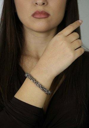 Bracciale a catena in argento con anelli circolari intrecciati, indossato al polso. La tonalità della pelle del modello è chiara, con una manica scura semplice visibile.
