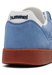 Blå mockaskor med en vit vadderad krage och en brun texturerad gummisula; "hummel"-logotypen på hälen i marinblå.