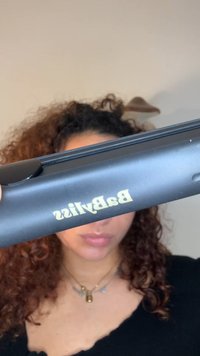 Sorte hårrettetang med gullbokstaver. Har et flatt design, glatt tekstur, og en liten knapp på siden for betjening.