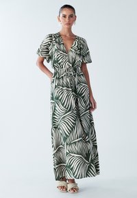 Maxikleit sügava V-kaeluse, lühikeste varrukate, vöökohast sõlmitud ja rohelise lehemustriga helel taustal. Kantakse punutud sandaalidega.