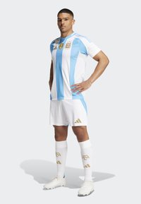 Vit fotbollströja med himmelblå vertikala ränder, guld detaljer, matchande shorts och knähöga vita strumpor med logodetalj.