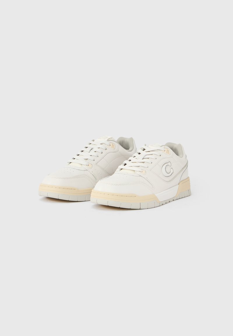 White leather sneakers with a low profile, round toe, light beige accents, textured surface, and cushioned sole. Logo on side.