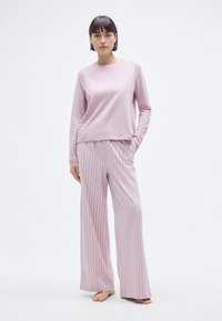 Haut à manches longues rose clair et pantalon de pyjama large à rayures. Tissu doux avec des rayures blanches horizontales sur le pantalon. Coupe décontractée. Pieds nus.