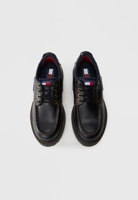 Scarpe in pelle nera con finitura liscia, punta tonda, cuciture marroni a contrasto, occhielli in metallo e interno blu navy imbottito.