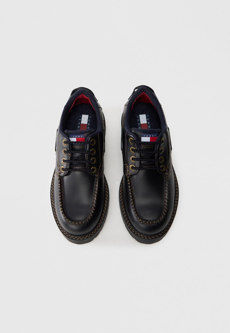 Chaussures noires en cuir avec une finition lisse, bout rond, couture contrastante marron, œillets en métal et intérieur rembourré bleu marine.