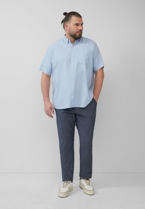 Chemise bleu clair à manches courtes avec col et poche avant, associée à un pantalon gris foncé et des baskets blanches décontractées.
