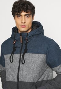 Hooded jacket featuring a blue and gray color block design, textured fabric, adjustable drawstrings, and a front zipper.