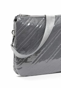 Bolso acolchado gris con acabado brillante. Presenta costuras diagonales, una correa plateada y una parte superior con cremallera. Forma compacta y rectangular.