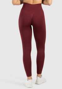 Bordeauxkleurige high-waisted leggings met een gestructureerd patroon, een aansluitend ontwerp en rekbare stof, gecombineerd met witte sportschoenen.