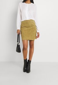 Blusa bianca a maniche lunghe con bordi in pizzo e bottoni, abbinata a una mini gonna in suede color sabbia. Stivali neri alla caviglia e una piccola borsa nera.