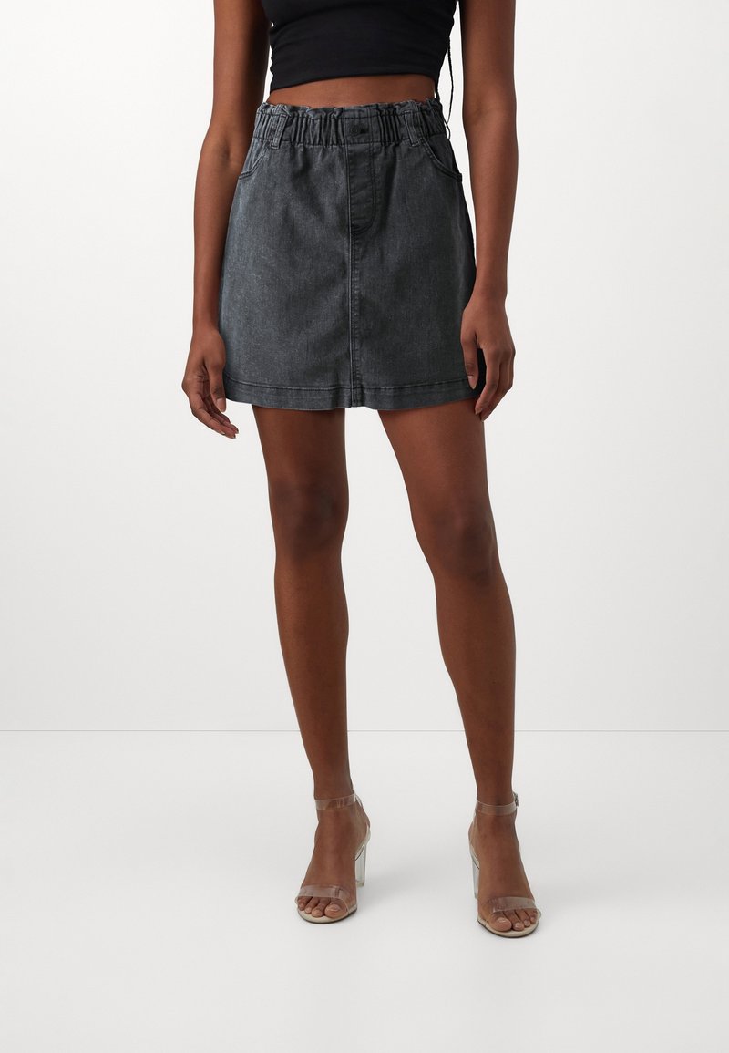 Mini gonna in denim nero con cintura elastica e tasche laterali, caratterizzata da una linea dritta e dettagli di cucitura minimi.