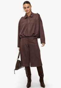 Veste zippée en suédine marron avec pantalon large assorti. Présente un col avec revers, des épaules tombantes et une coupe décontractée.