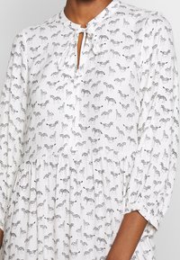 Vitt klänning med svarta zebramönster, rund halsringning med nyckelhålöppning och långa ärmar med rynkade detaljer vid manschetterna.