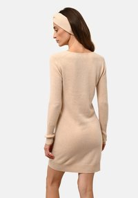 Abito a maglia beige con maniche lunghe, polsini e orlo in costina. Texture morbida e forma aderente, abbinato a un cerchietto coordinato.