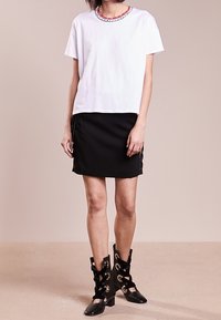 Vit bomullströja med en färgglad broderad halsringning, i kombination med en svart kjol med sidolacingdetaljer och svarta klackstövlar.