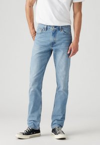 Világoskék farmernadrág egyenes szabással, öt zsebbel és kontrasztos varrási részletekkel, fekete sneaker cipővel párosítva.