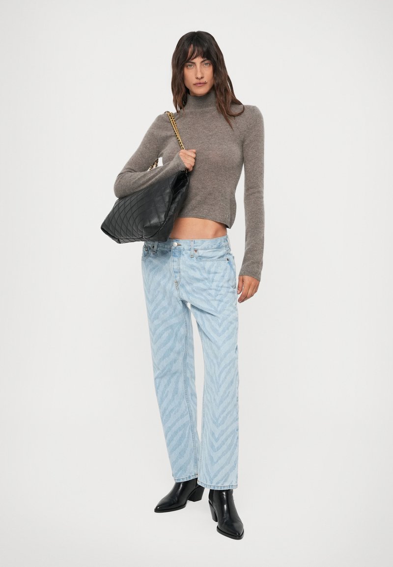 Vrouw in een grijze coltrui, lichtblauwe gebloemde jeans, zwarte enkellaarsjes, met een zwart gewatteerd handtas met een gouden schouderband.