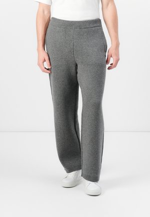 Gray knit sweatpants with a wide waistband and side pockets, featuring a soft texture and a relaxed fit, paired with white sneakers.