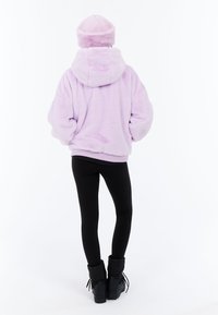 Lila yöpaita, jossa on korkea kaulus ja yhteensopiva hattu, yhdistettynä mustiin legginsseihin ja mustiin talvikenkään, nähtynä takaa.