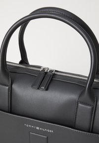 Black leather handbag with a structured design, featuring two round handles, silver zipper, and a subtle brand logo at the bottom.