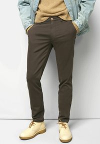 Bruine katoenen broek met een slim fit, voorzien van een knoopsluiting, zijzakken en gedragen met lichtbeige schoenen.