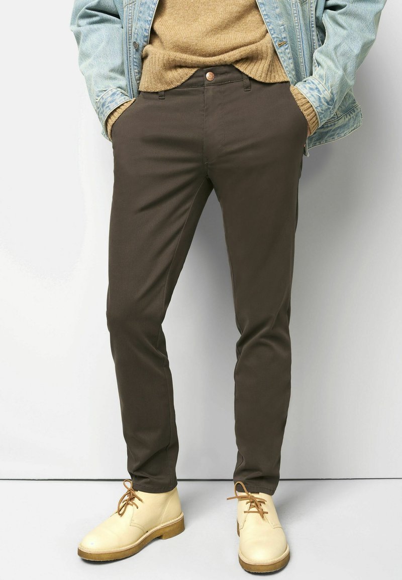 Bruine katoenen broek met een slim fit, voorzien van een knoopsluiting, zijzakken en gedragen met lichtbeige schoenen.