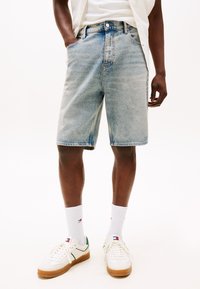 Light blue denim shorts feature a relaxed fit, five-pocket design, and contrast stitching. Paired with white sneakers and ribbed socks.