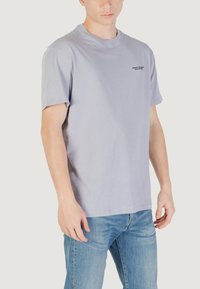 T-shirt grigia a maniche corte con scollatura rotonda, caratterizzata da un logo nero discreto sul petto. Realizzata in morbido cotone.