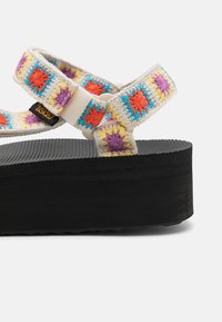 Sandale plateforme noire avec des brides en crochet multicolores présentant des motifs d'étoiles. Les brides sont fixées avec des accessoires en plastique. Semelle intérieure texturée.