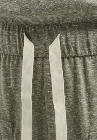 Pantalons de survêtement vert olive avec une texture douce, dotés d'une taille froncée et de cordons de serrage couleur crème. Comprend des poches latérales.