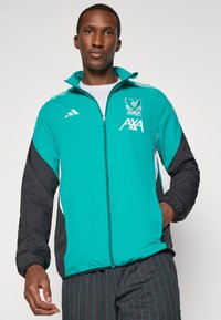 Teal og sort vindjakke med fuld lynlås, hvide accenter og broderet logo. Lavet af letvægts, vandafvisende materiale.