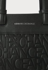 Black textured handbag featuring embossed "Armani Exchange" logo, smooth handles, and a structured design, emphasizing luxury and durability.