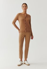 Bruine cardigan met knopen, gecombineerd met tan slim-fit broek en witte sneakers. Soepele textuur, eenvoudig ontwerp en een relaxte pasvorm.