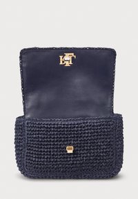 Μπλε τσάντα από ύφασμα με υφή και λείο δερμάτινο καπάκι; διαθέτει χρυσό λογότυπο και αξεσουάρ, συμπαγές ορθογώνιο σχήμα.