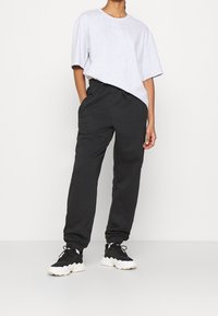 Grå oversized t-shirt, avslappnad passform, rund hals. Svarta joggerbyxor med elastiska muddar, sidofickor. Bärs med svart och vit sneakers.