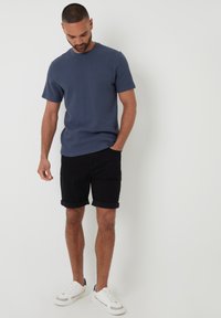 Modrá texturovaná trička, černé zkrácené kraťasy, bílé tenisky s černými akcenty. Neformální letní outfit s volným střihem a jednoduchým designem.