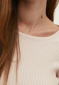 Hellrosa gerippter Pullover mit einem weiten Ausschnitt und schrägen Nähdetails an den Schultern. Weicher Stoff mit einer taillierten Passform.