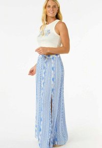 Falda maxi de tela azul con patrones tribales blancos. Presenta una gran abertura y un ajuste holgado, combinada con una blusa sin mangas blanca.