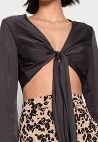 Haut en satin noir à manches longues, présentant un devant noué et des côtés découpés, associé à une jupe beige avec un motif léopard noir.