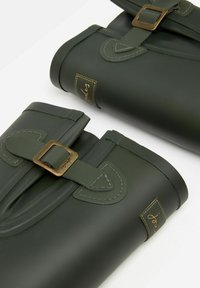 Ciemnozielone gumowe kalosze z gładką fakturą, z brązowymi klamrami i przeszyciami. Naszywka z logo po boku.