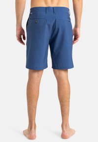 Modré šortky s textúrovanou tkaninou, rovný predný strih, dve zadné vrecká a malá logo nášivka pri páse.