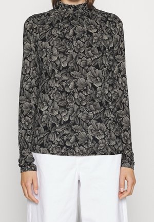 Black long-sleeve top with high ruffled neck, featuring an abstract floral pattern in white lines, paired with white pants.