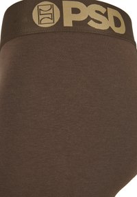 Close-up van de bruine onderbroeksband met het beige PSD-logo en cirkelvormig ontwerp op de stof.