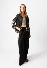 Čierna ľahká bunda s kvetinovým vzorom, béžová priliehavá rebrovaná blúzka a široké čierne nohavice. Hladká textúra a uvoľnený strih.