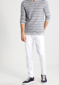 Grå och marinrandig långärmad skjorta med rund hals, kombinerad med vita slim-fit byxor och marinblå sneakers med vita snören och röda detaljer.